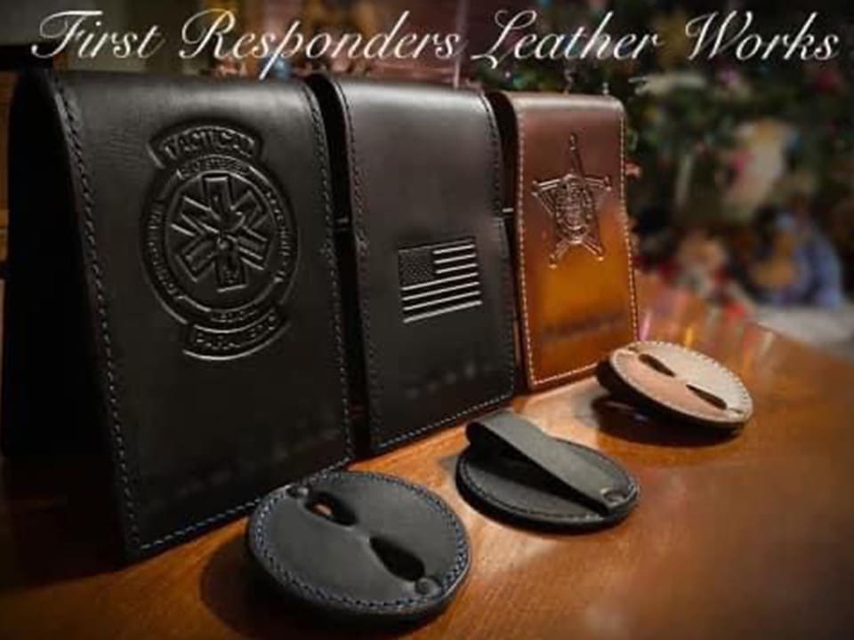 Three leather Badge Holder (Loop) pouches with embossed designs—a medical symbol, U.S. flag, and sheriff’s badge—are displayed on a wooden surface, with additional leather key holders in front.